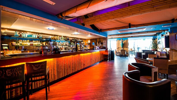 Zona bar con pavimento in legno, bancone e posti a sedere.