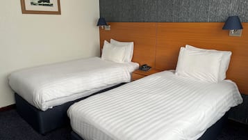 Ett hotellrum med två separata sängar, en sänggavel i trä, en inramad tavla på väggen och två vägglampor.