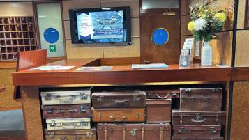 A reception desk with a television displaying a wedding open day event, a vase with flowers, and vintage suitcases stacked below.