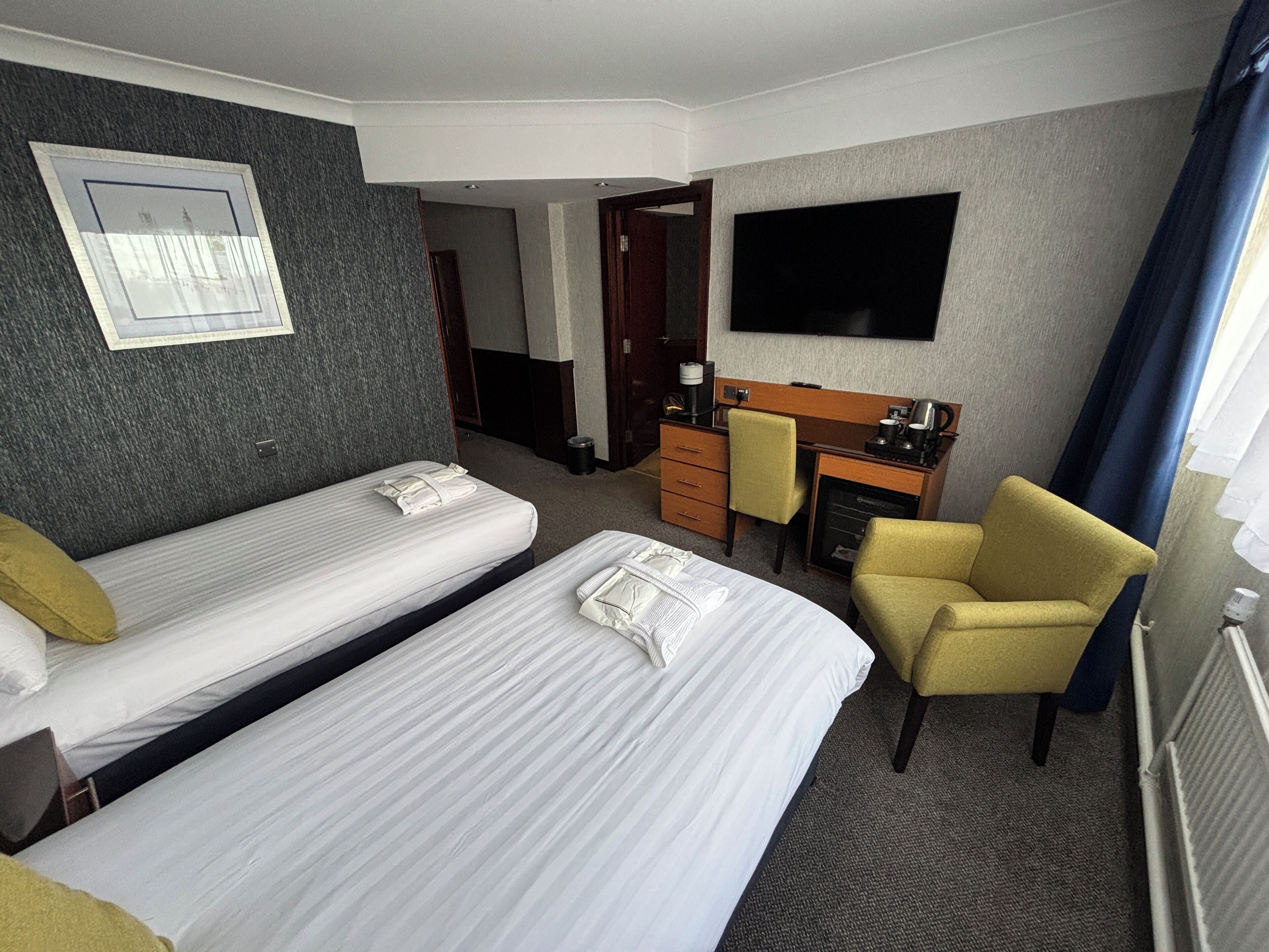 A hotel room with two single beds, a desk, a chair, a television, and a window with curtains.