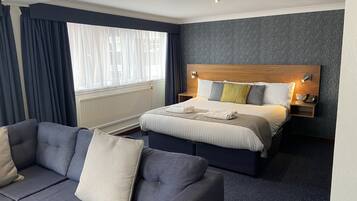 Una habitación de hotel con cama, sofá, mesita de noche y ventana con cortinas.