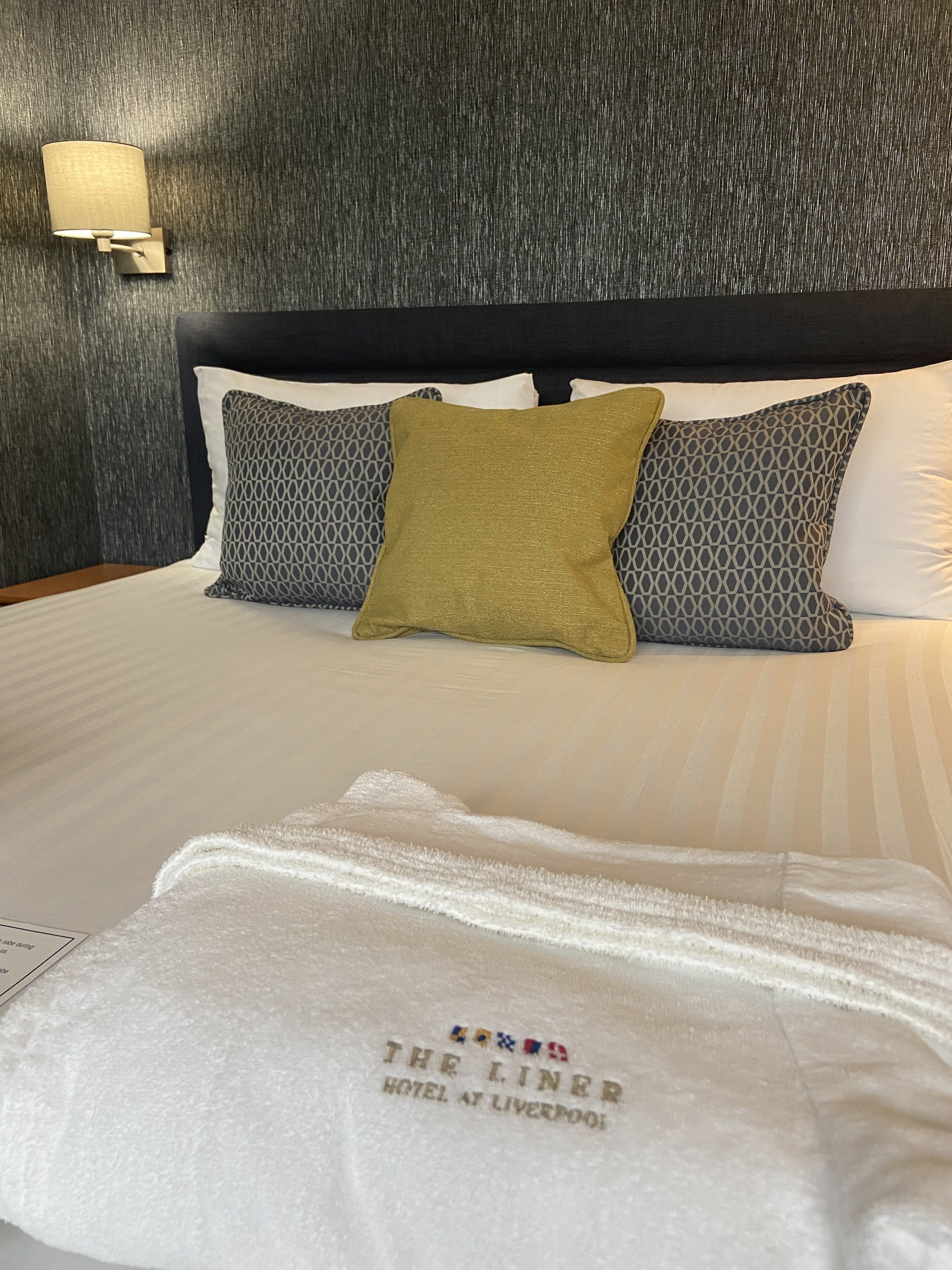 A hotel room with a bed, pillows, and a towel with the hotel name.