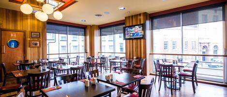 A restaurant with multiple tables and chairs, large windows, and a television screen.