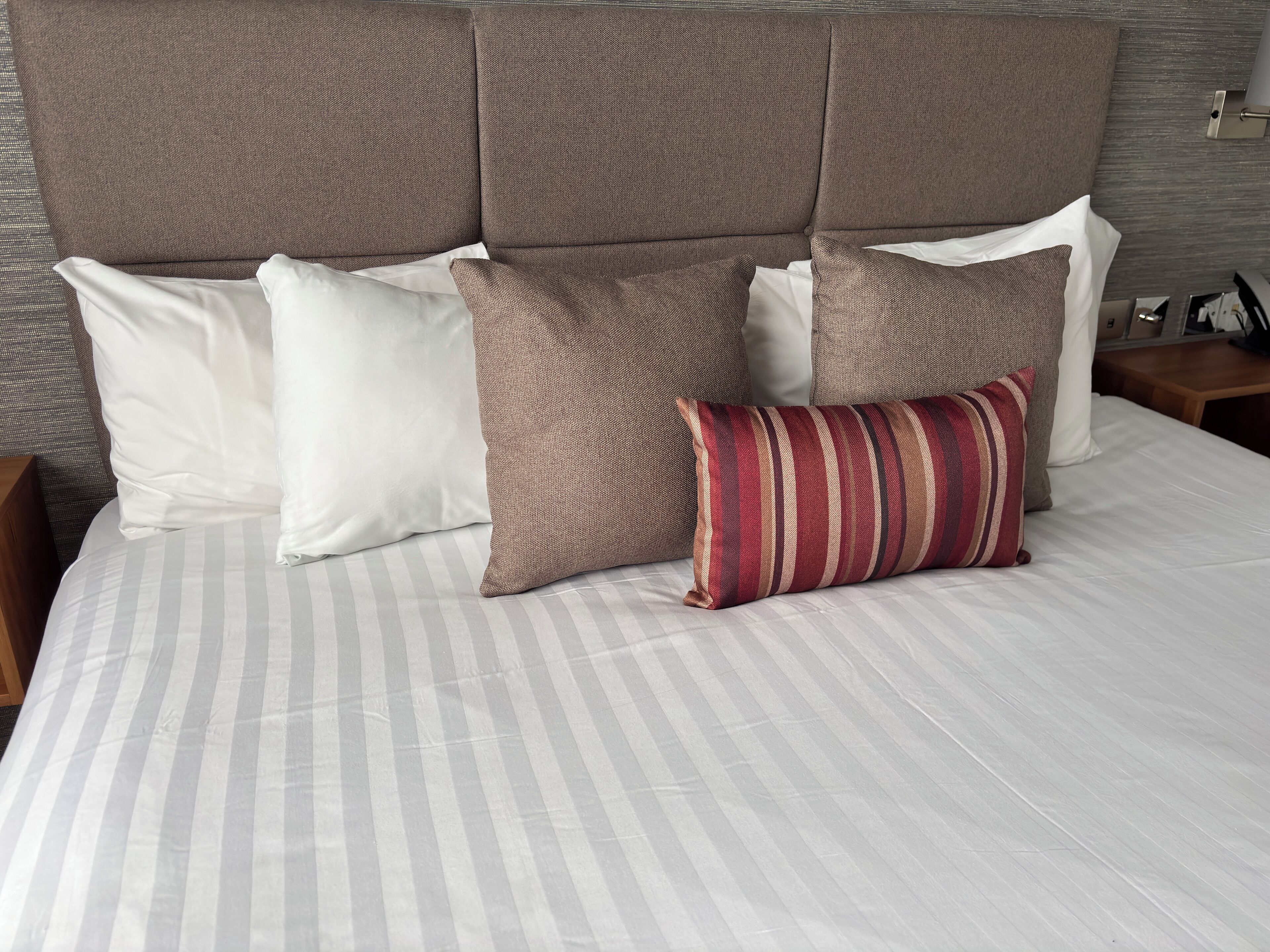Un letto rifatto con cura, con lenzuola a righe, una testiera e diversi cuscini di vari colori e fantasie.
