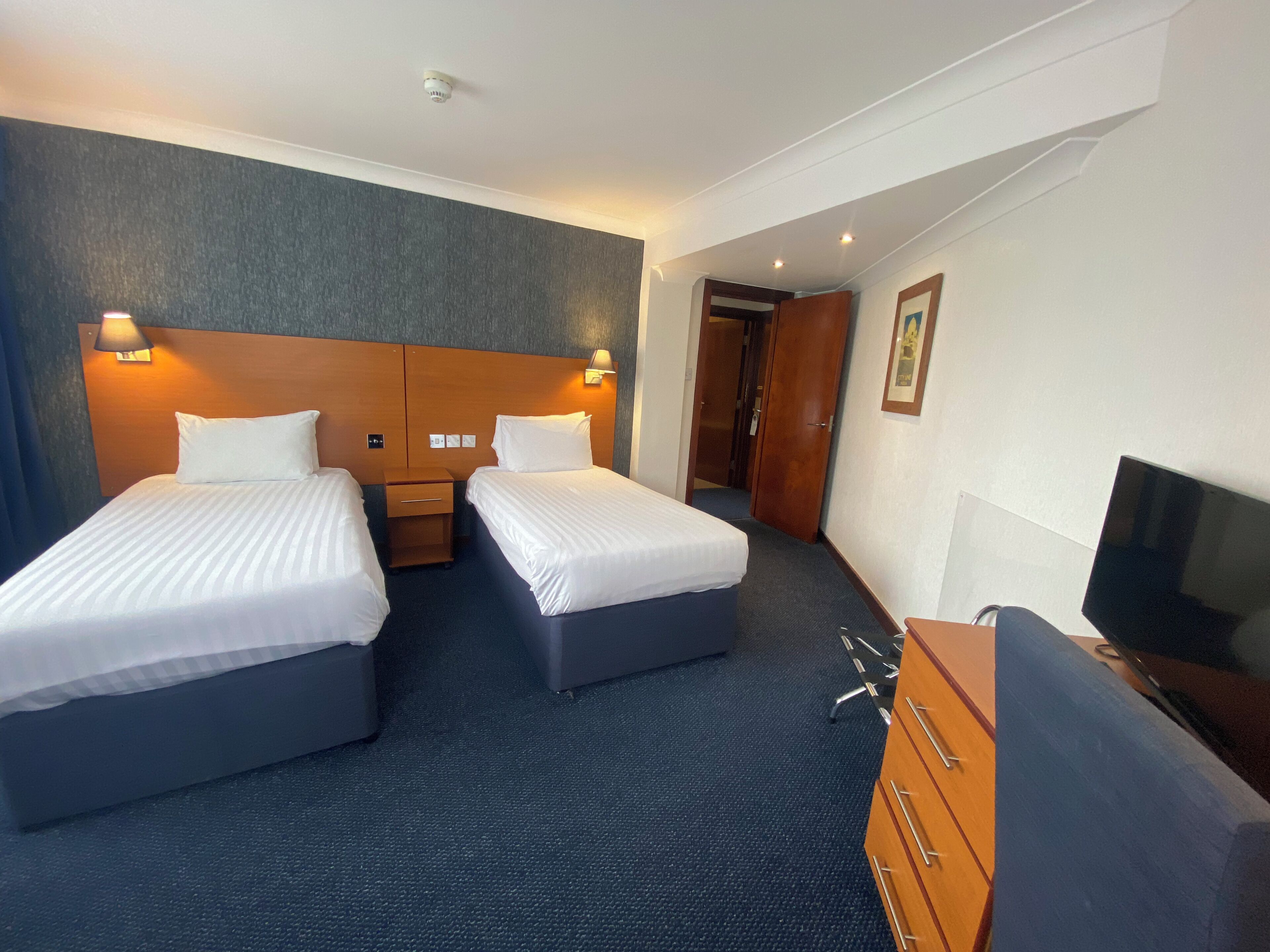 A hotel room with two beds, a wooden dresser, a television, and a door leading to another room.