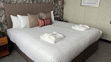 A neatly made bed with white linens and striped pillows, a headboard, and a framed picture on the wall.