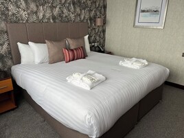Una cama bien hecha con sábanas blancas y almohadas a rayas, un cabecero y un cuadro en la pared.