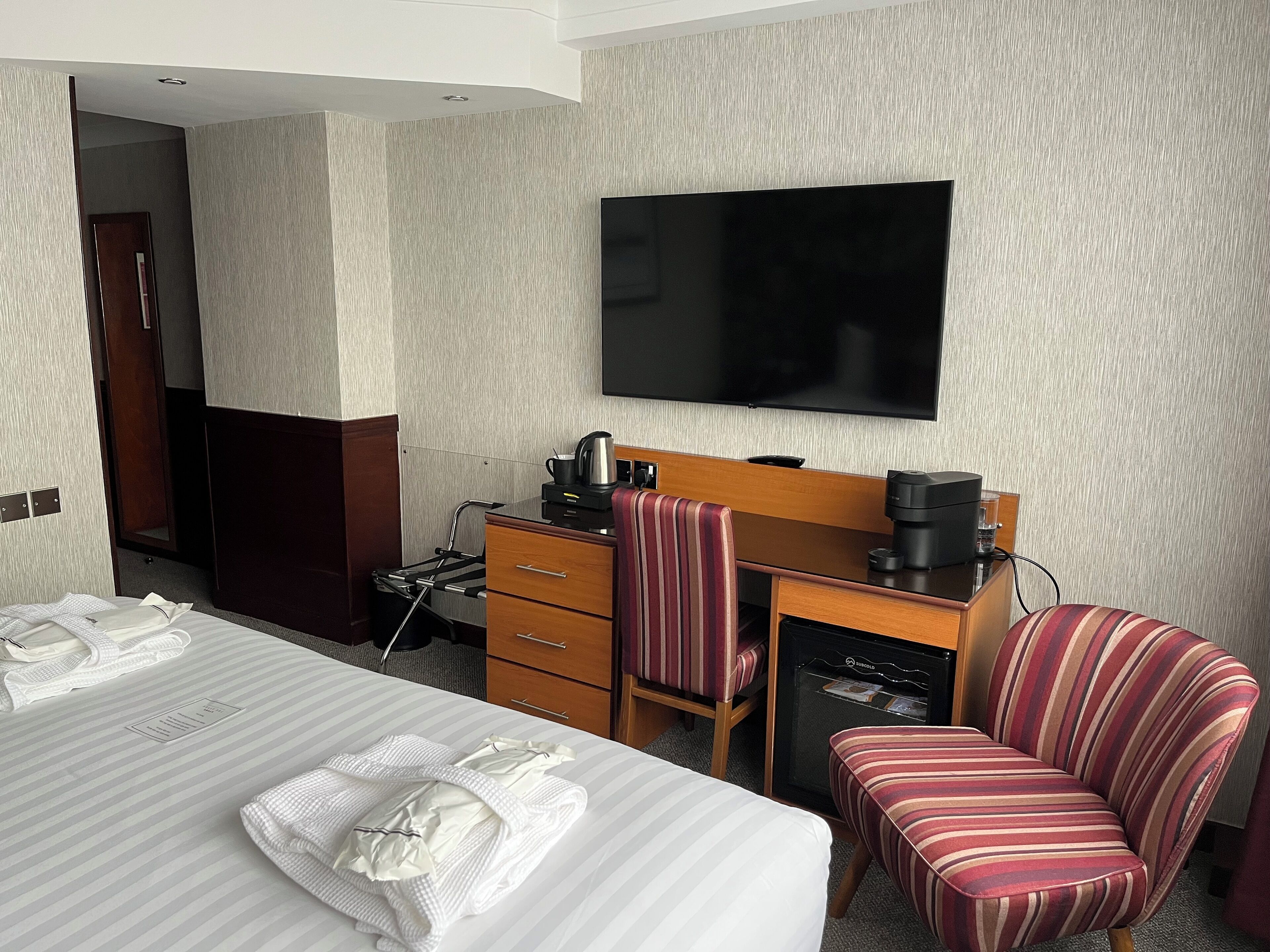Ein Hotelzimmer mit Bett, Schreibtisch mit Stuhl, Fernseher und einer Minibar.