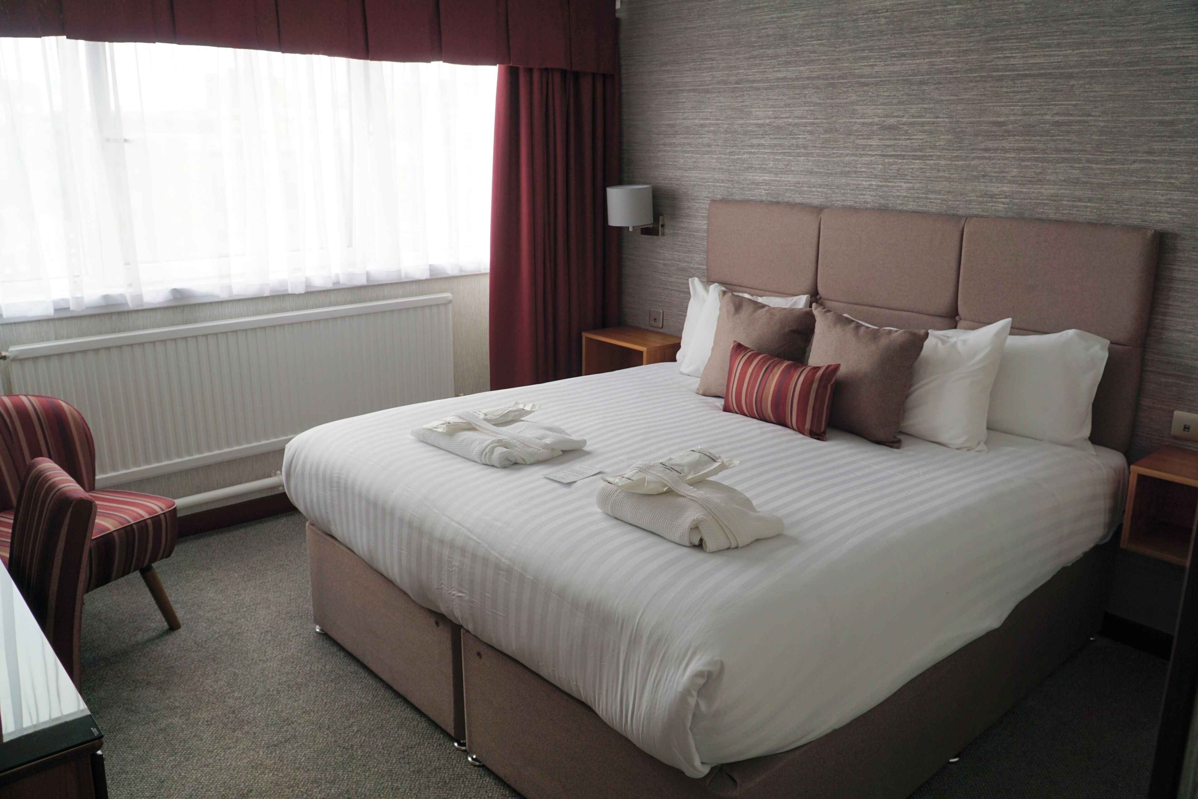 A hotel room with a large bed, a bedside table, a chair, and a window with curtains.