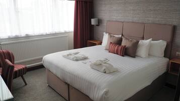A hotel room with a large bed, a bedside table, a chair, and a window with curtains.