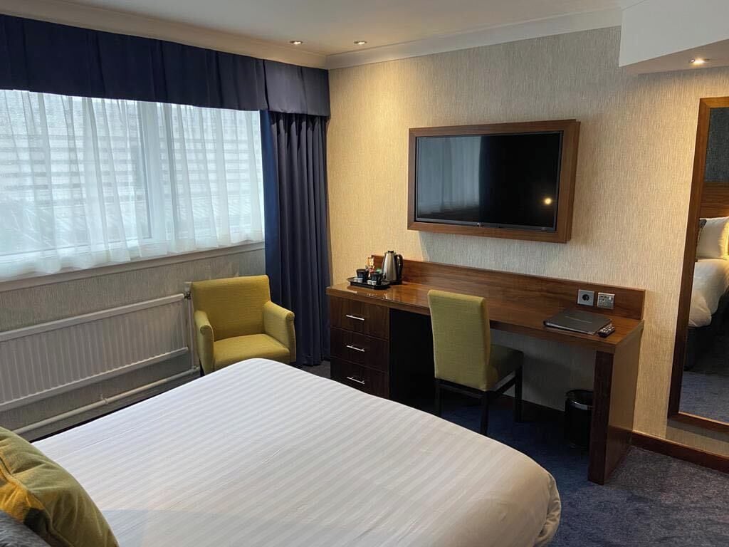 A hotel room with a bed, a desk, a chair, a television, and a window with curtains.