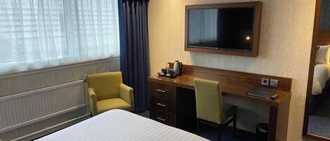 Une chambre d’hôtel équipée d’un lit, d’un bureau, d’une chaise, d’une télévision et d’une fenêtre avec des rideaux.