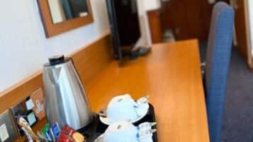 A hotel room with a wooden table set with a coffee pot, tea cups, and a tray of snacks.