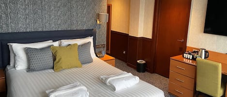 Una habitación de hotel con una cama grande, un escritorio, una silla, un armario, un televisor y una lámpara.