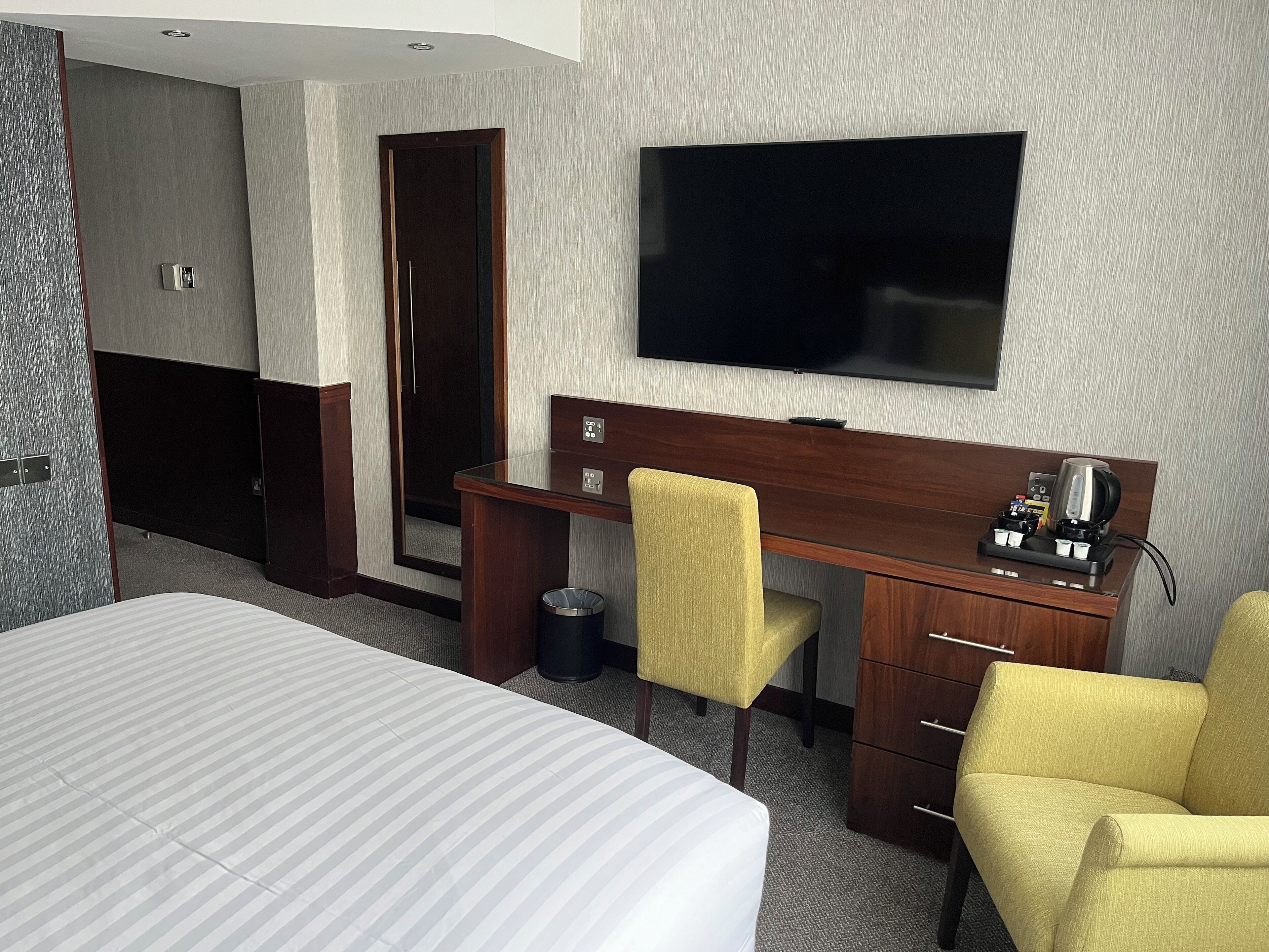 Ein Hotelzimmer mit einem Bett, einem Schreibtisch mit Stuhl, einem Fernseher und einer Kaffeemaschine.