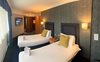 Habitación de hotel con dos camas, un televisor en la pared y una mesita con un control remoto.