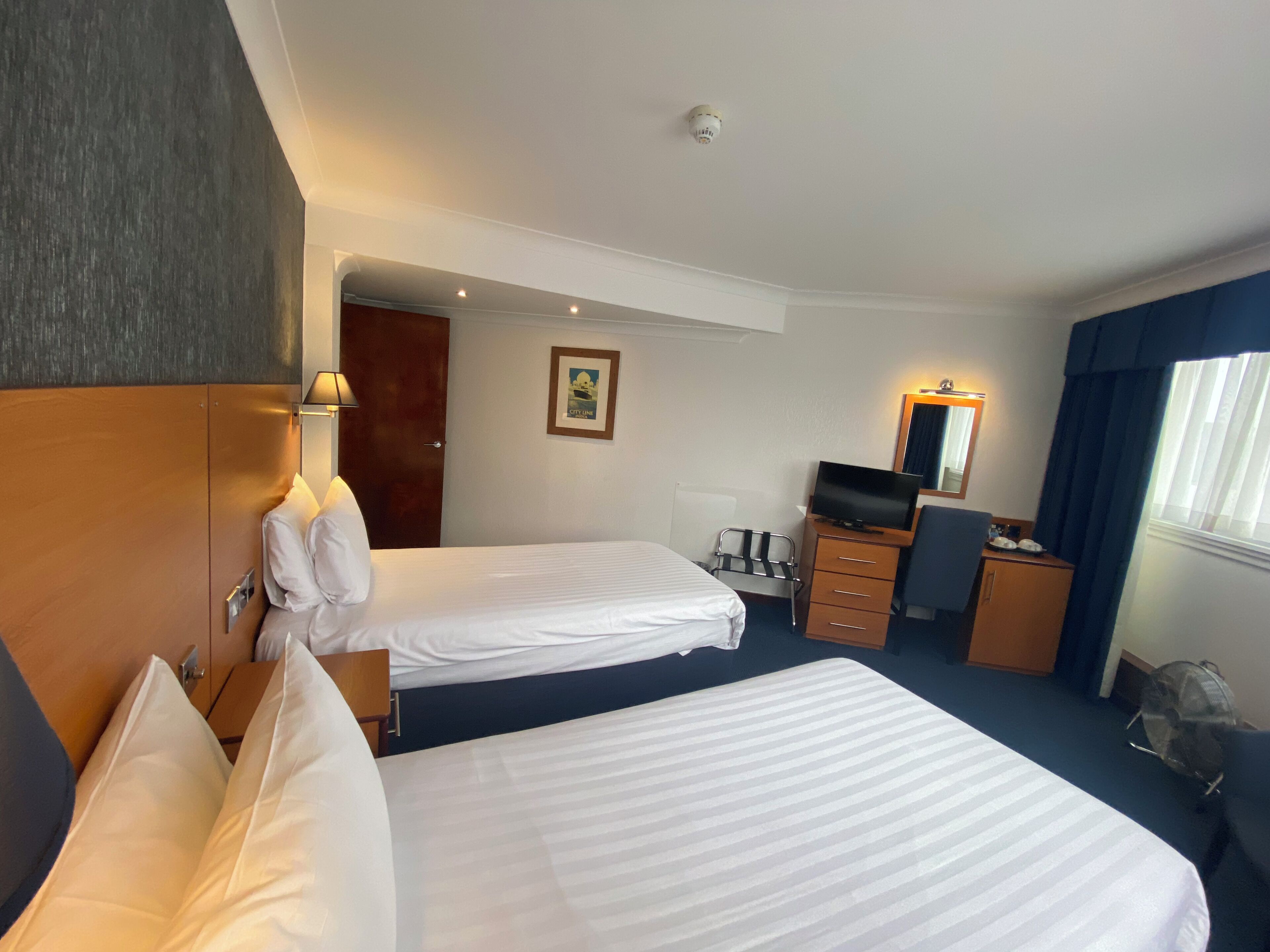 A hotel room with two beds, a desk, a television, and a mirror.