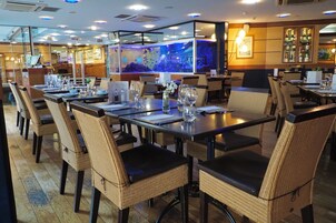 A restaurant with multiple tables and wicker chairs, a large aquarium, and a bar area with bottles and glasses.