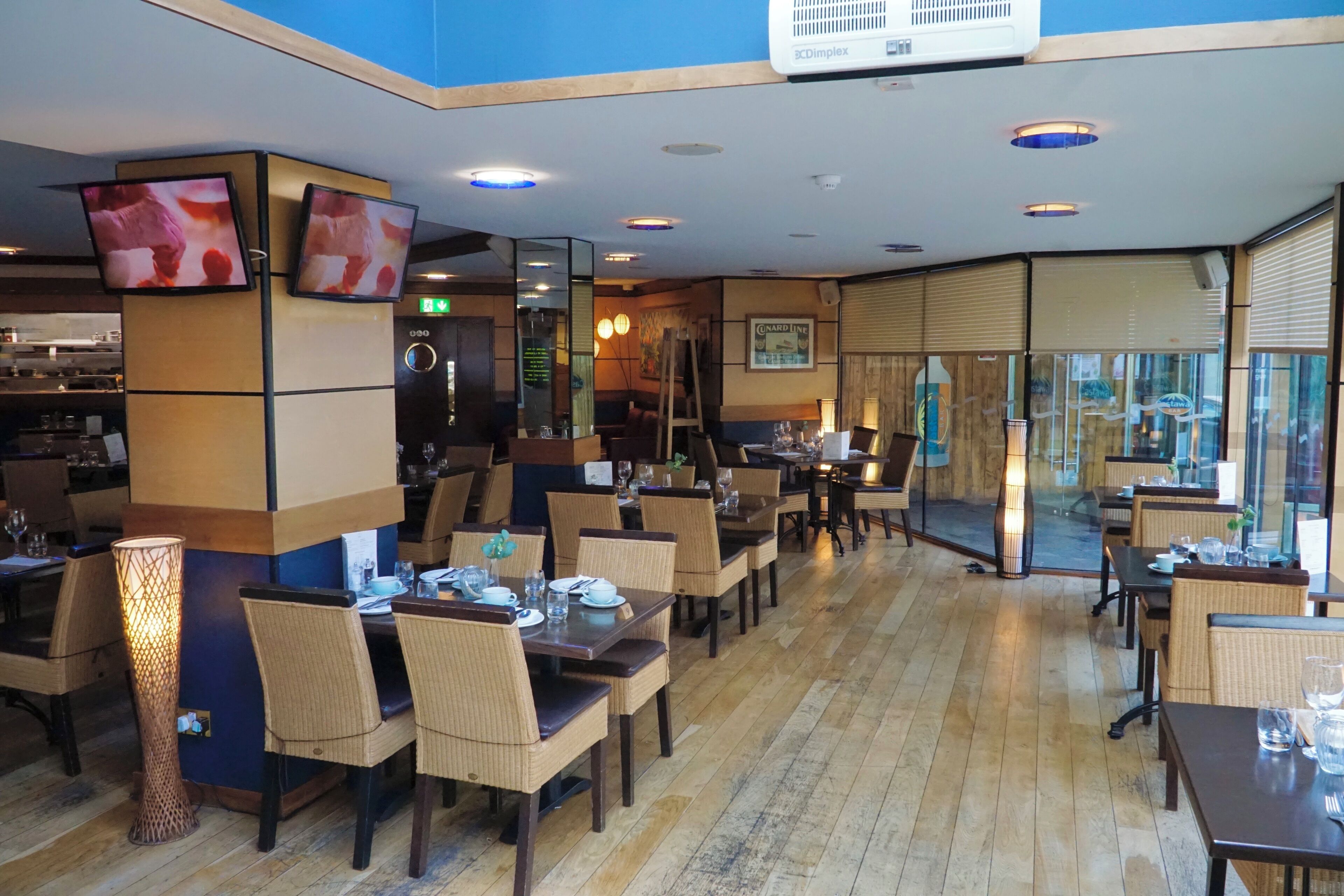 Un restaurante con suelo de madera, varias mesas y sillas, y un televisor en la pared.