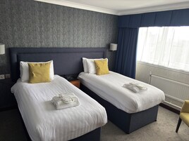 Una habitación de hotel con dos camas, una mesita de noche, una lámpara y una ventana con cortinas.