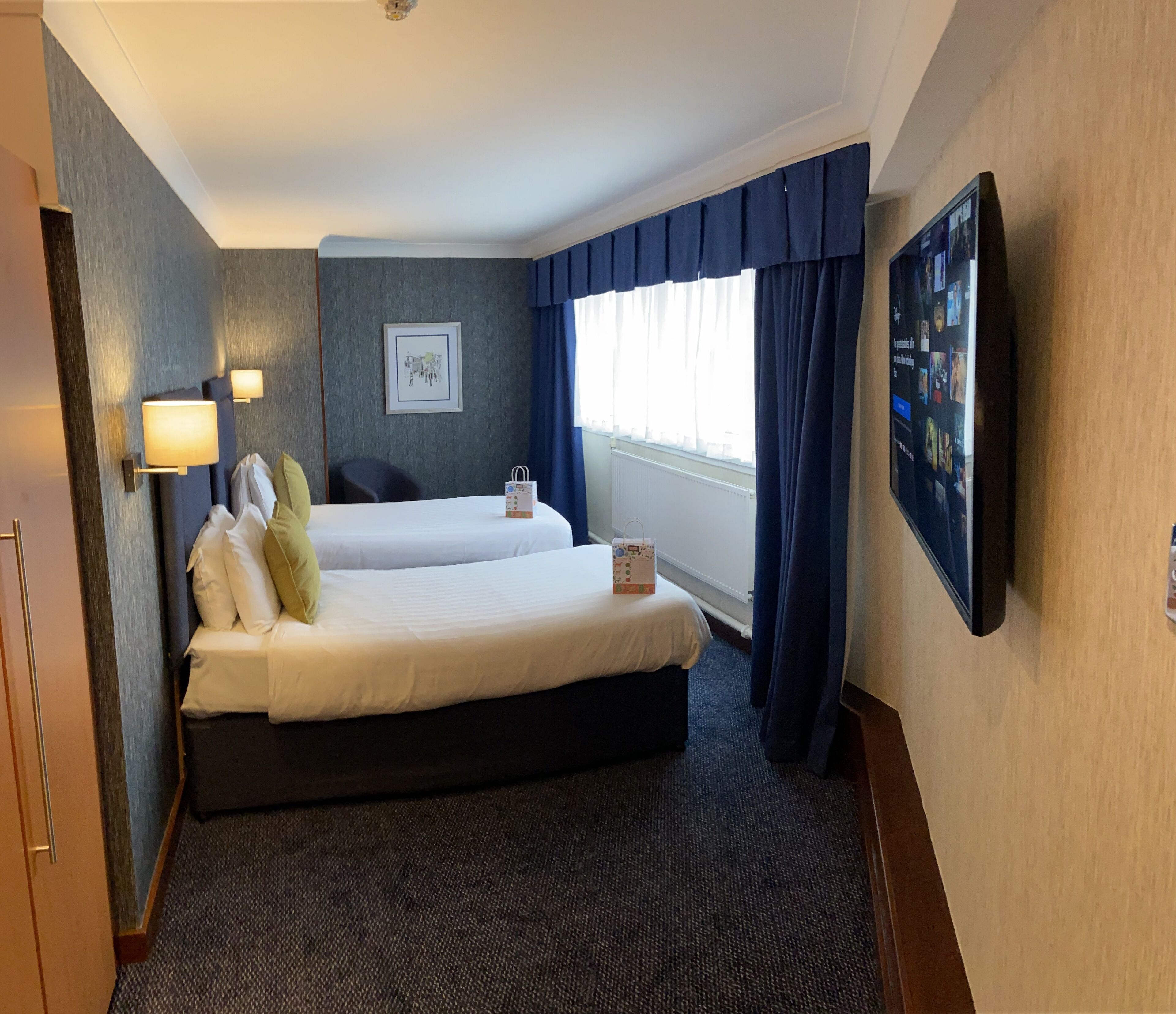 A hotel room with two beds, a flat-screen TV, a framed picture on the wall, and a window with curtains.