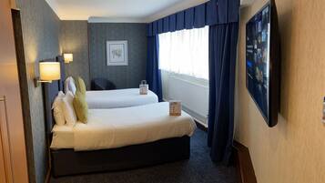 A hotel room with two beds, a flat-screen TV, a framed picture on the wall, and a window with curtains.