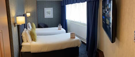 A hotel room with two beds, a flat-screen TV, a framed picture on the wall, and a window with curtains.