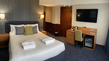 Una habitación de hotel con una cama grande, un escritorio, un televisor y un minibar.