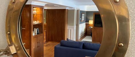 A round brass ship's porthole mirror reflecting a room with a blue sofa, wooden cabinets, and a lamp.