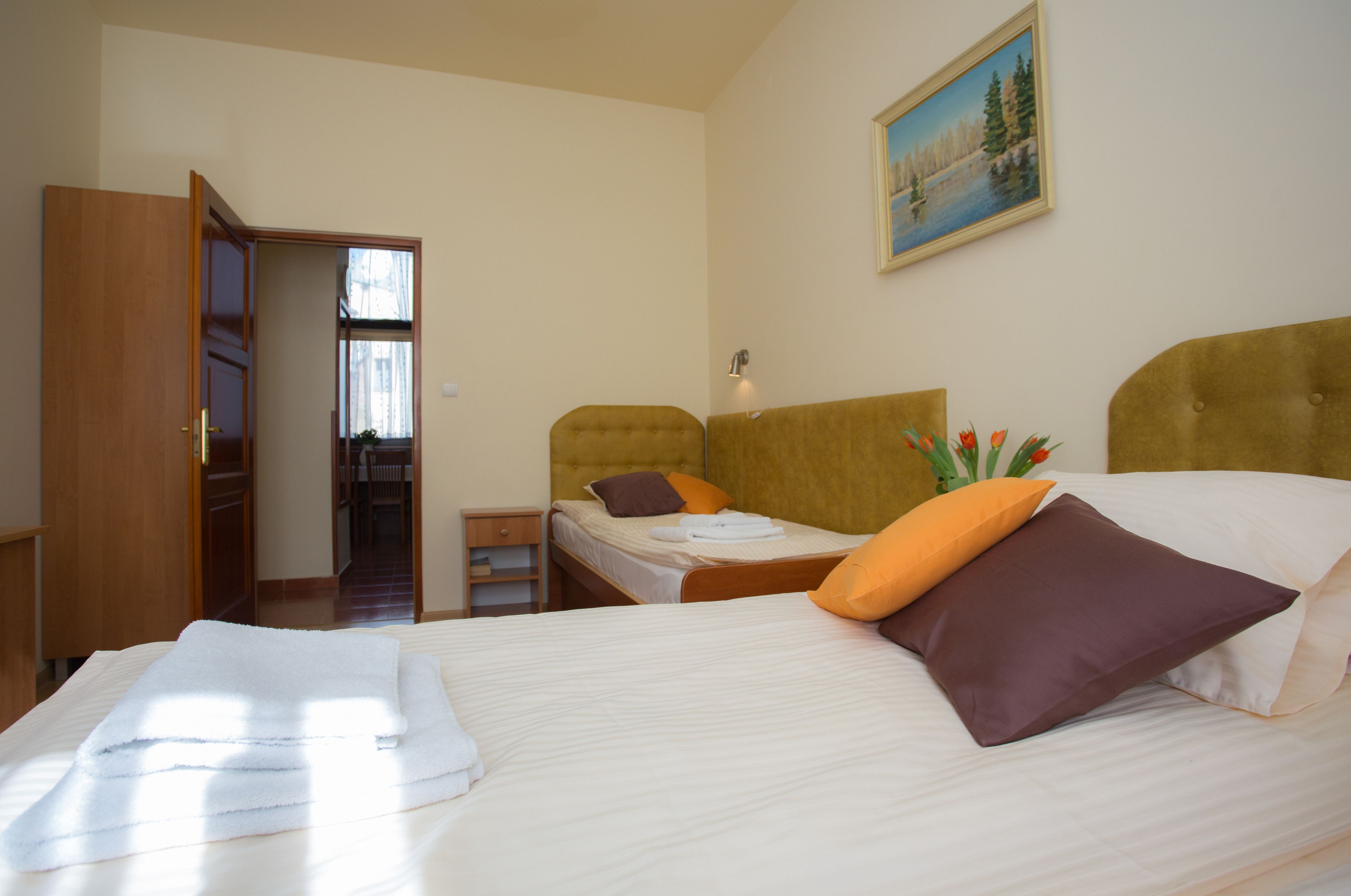 A hotel room with a large bed, a smaller bed, a wardrobe, and a painting on the wall.