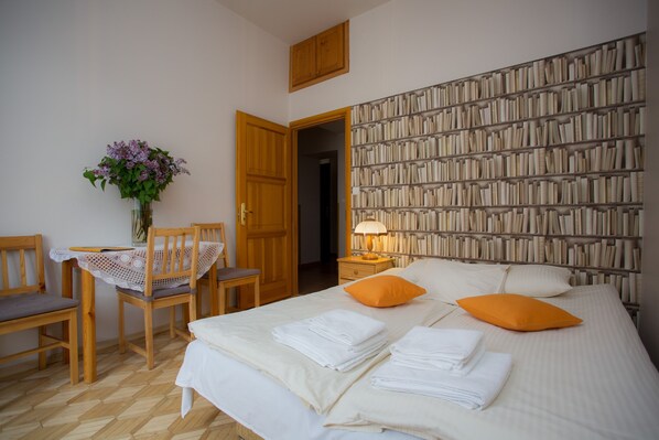 A neatly arranged bedroom with a bed, pillows, a bedside table, a chair, and a bookshelf. - Kazimierz's Secret Apartments (Kraków)