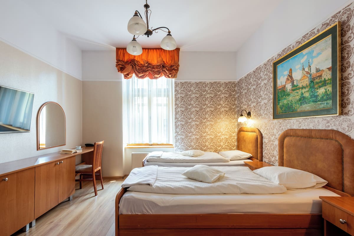 Ein Hotelzimmer mit zwei Betten, einem Schreibtisch, einem Sessel, einem Fernseher und einem Bild an der Wand.