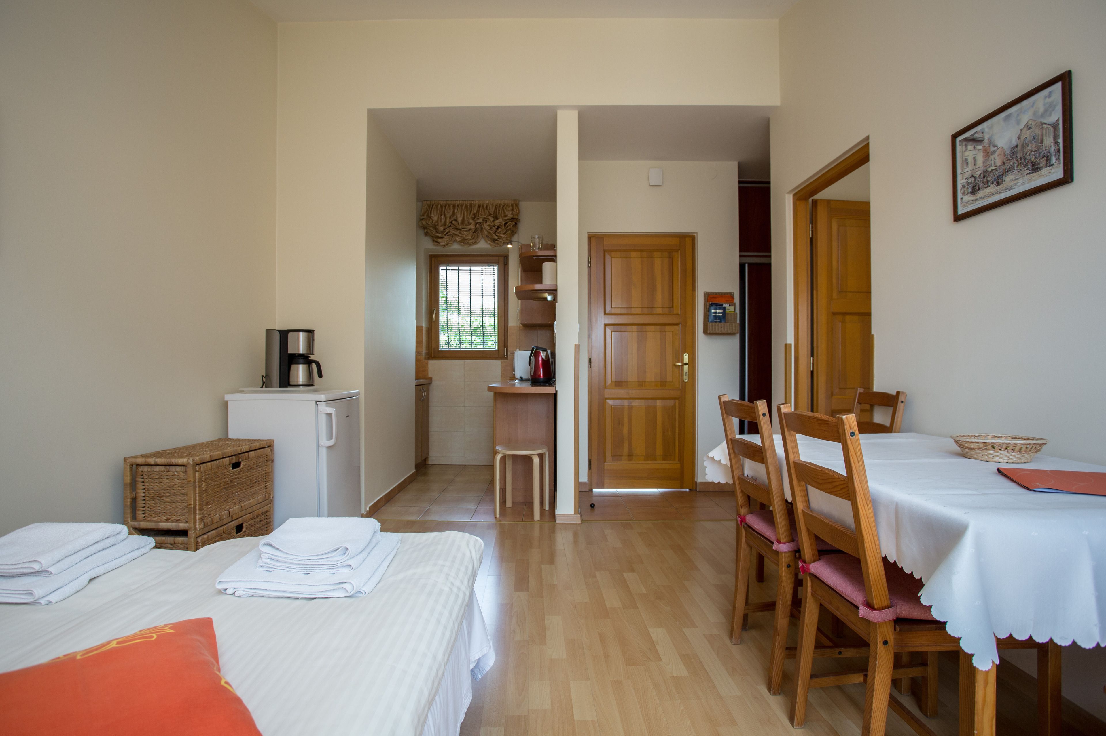 A hotel room with a bed, a desk, a coffee machine, a refrigerator, and a dining area with chairs and a table.
