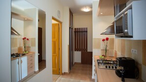 Cozinha moderna com fogão, micro-ondas e forno. Uma porta de madeira dá acesso a outro espaço.