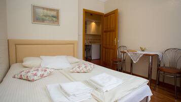 Una cama bien hecha con almohadas, una mesita con mantel de encaje y una silla.