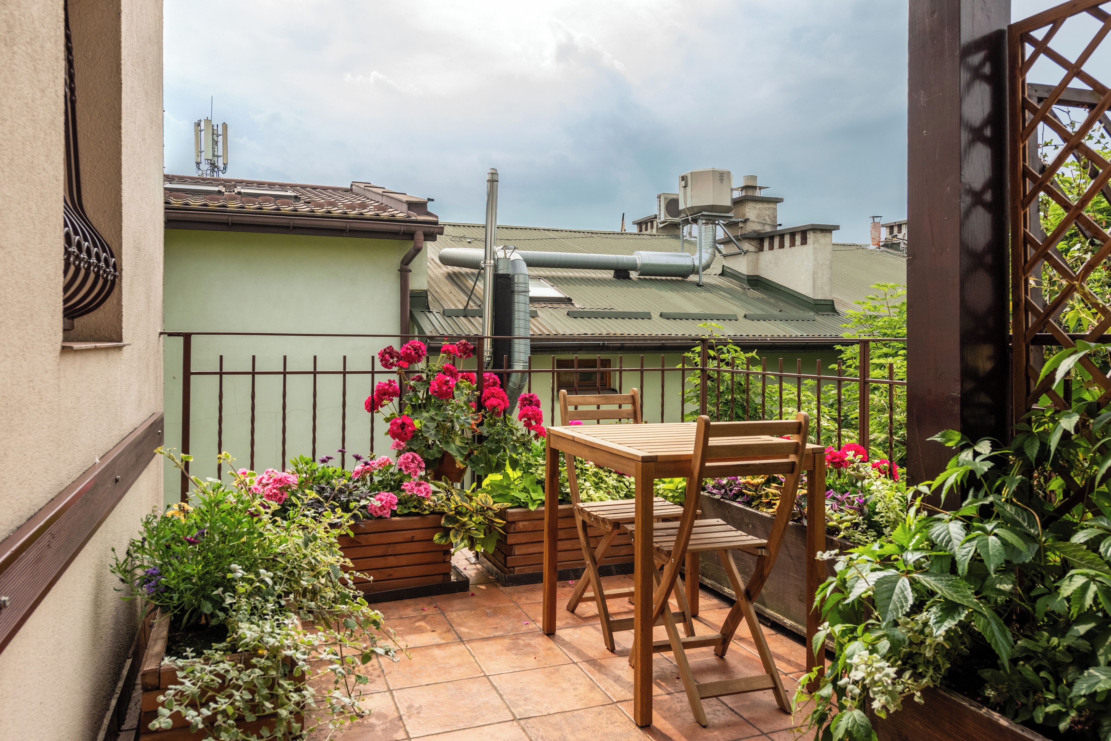 En balkon med et træbord og stole, omgivet af krukker med planter og blomster.