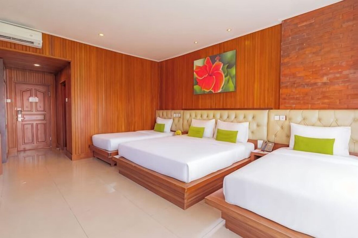A hotel room with three beds, wooden paneling, a large floral artwork, and a wooden door.