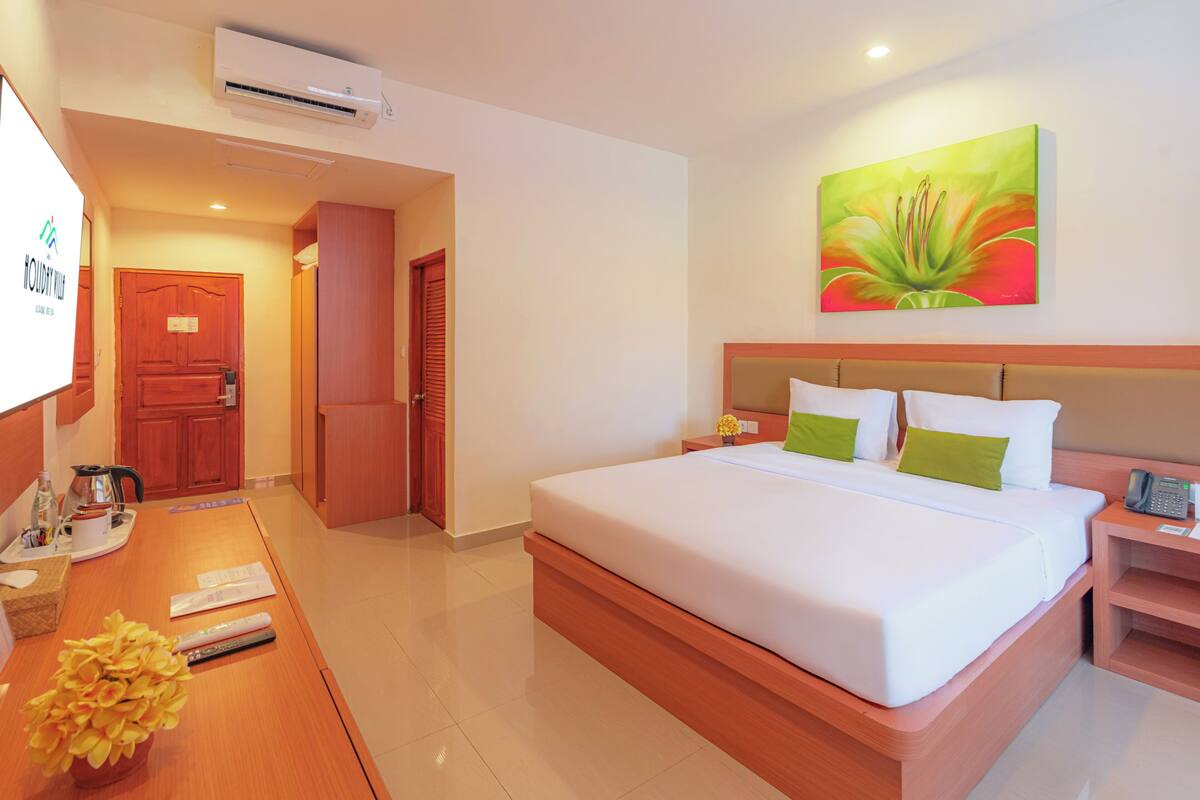 Quarto de hotel com uma cama grande, uma escrivaninha com um laptop, telefone e um quadro na parede.