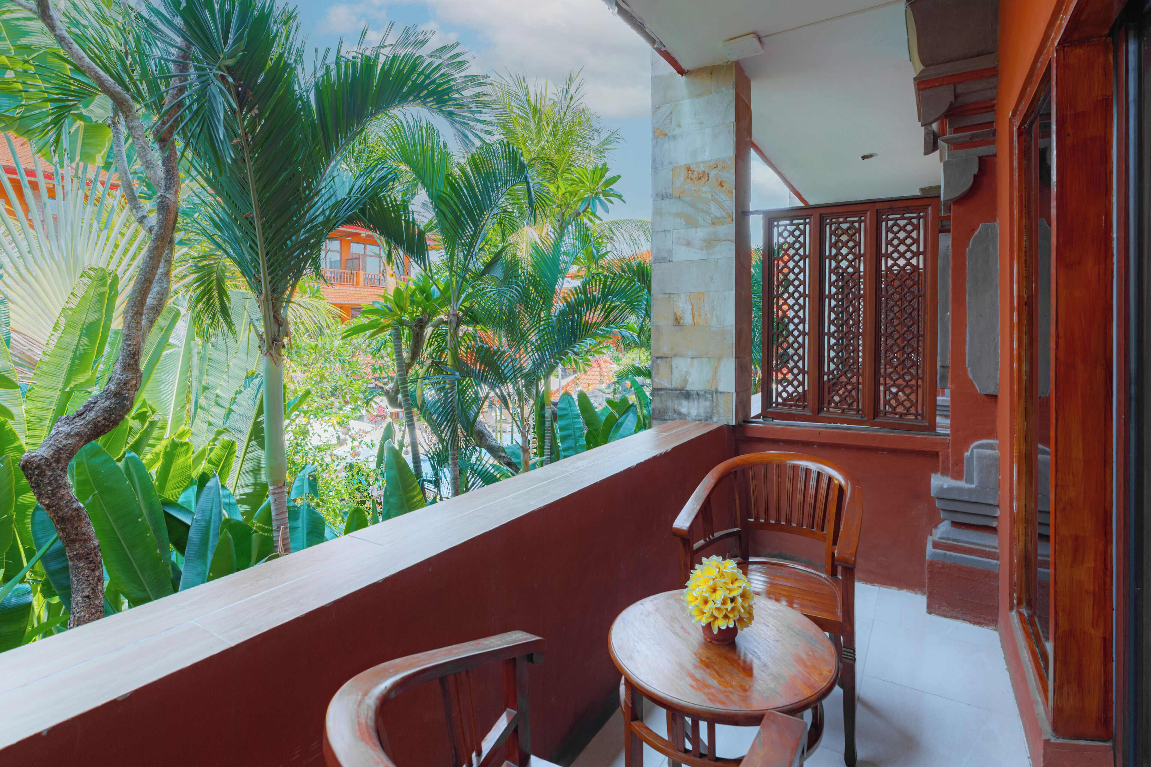 A balcony with a table and chairs, a view of lush greenery, and traditional wooden lattice partition.