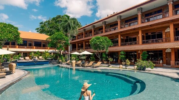 A pool area with a person sitting by the pool, surrounded by lounge chairs and umbrellas. - Wina Holiday Villa (Kuta)