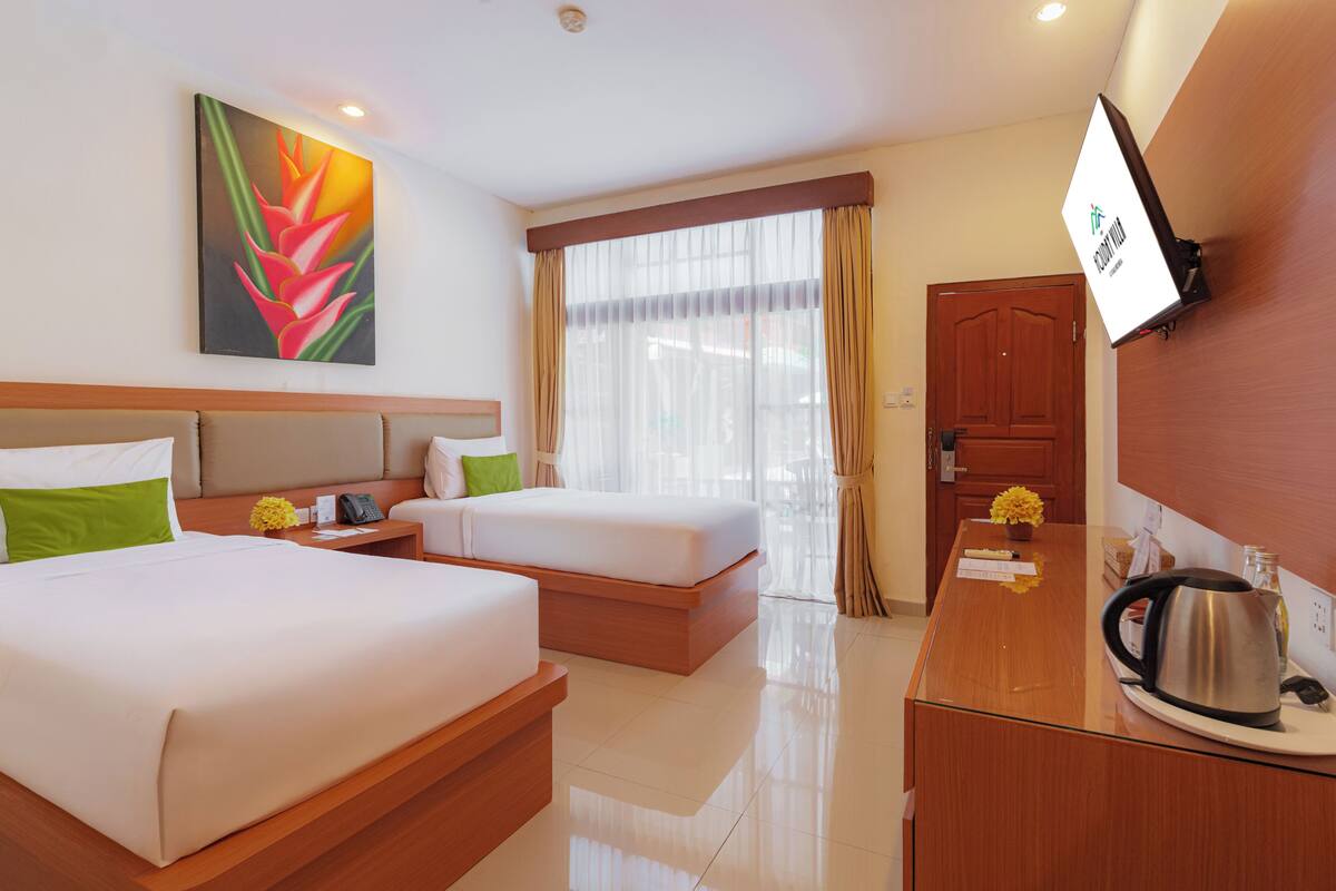 Quarto de hotel com duas camas, uma mesa com chaleira, televisão e uma janela grande com cortinas.