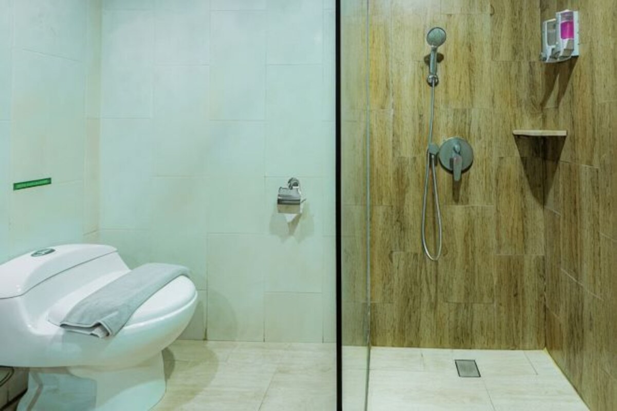 Un baño con inodoro, ducha con pared de madera y un estante pequeño con artículos de aseo.