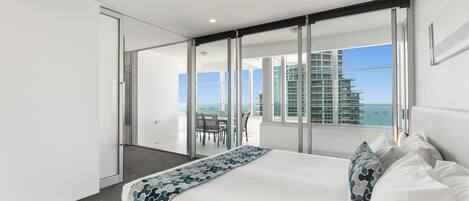 Une chambre d’hôtel moderne dotée d’un grand lit, d’un balcon offrant une vue sur la ville et d’une porte-fenêtre coulissante donnant sur un espace extérieur.