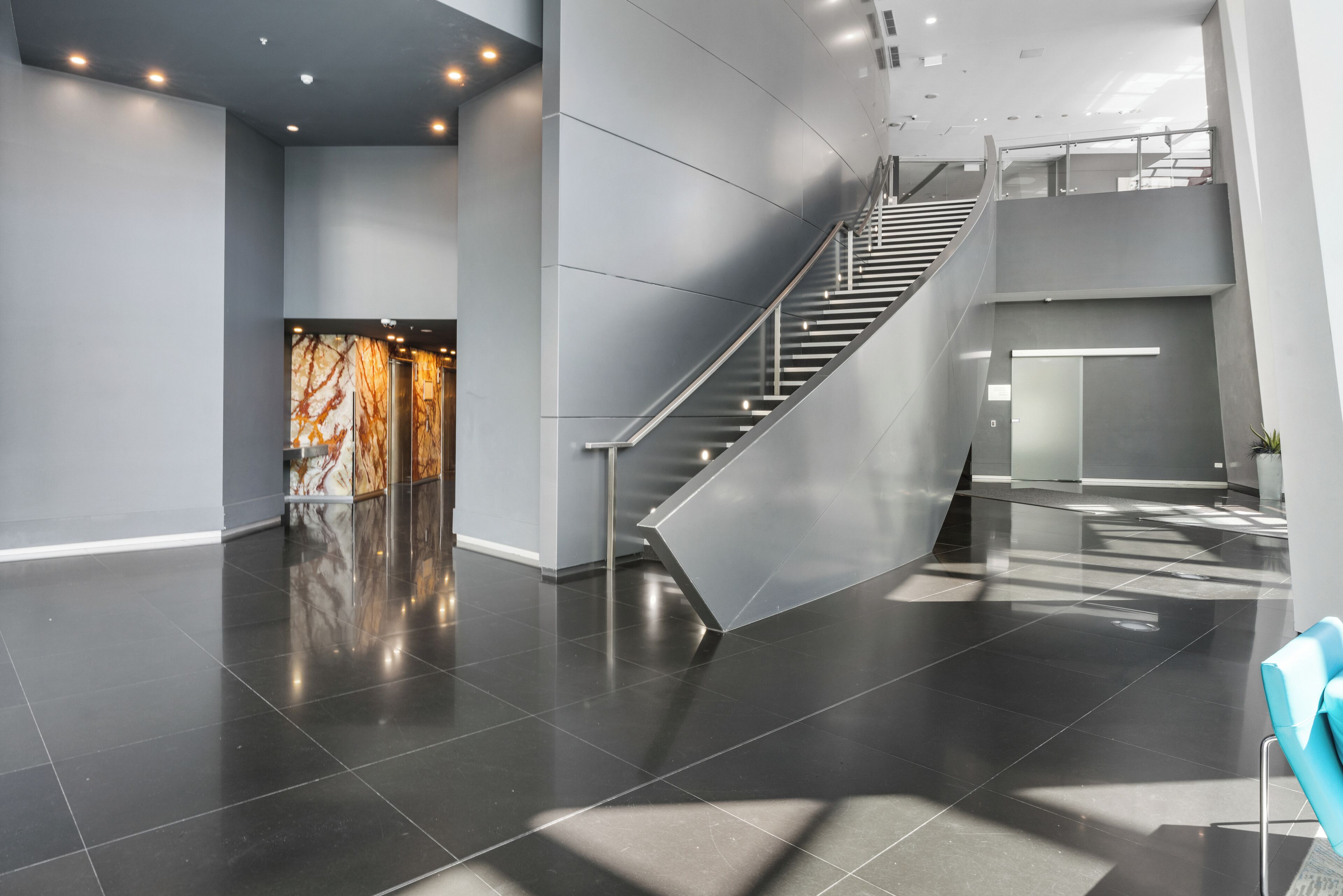 A modern lobby with a glass staircase, polished dark floors, and a marble reception desk.