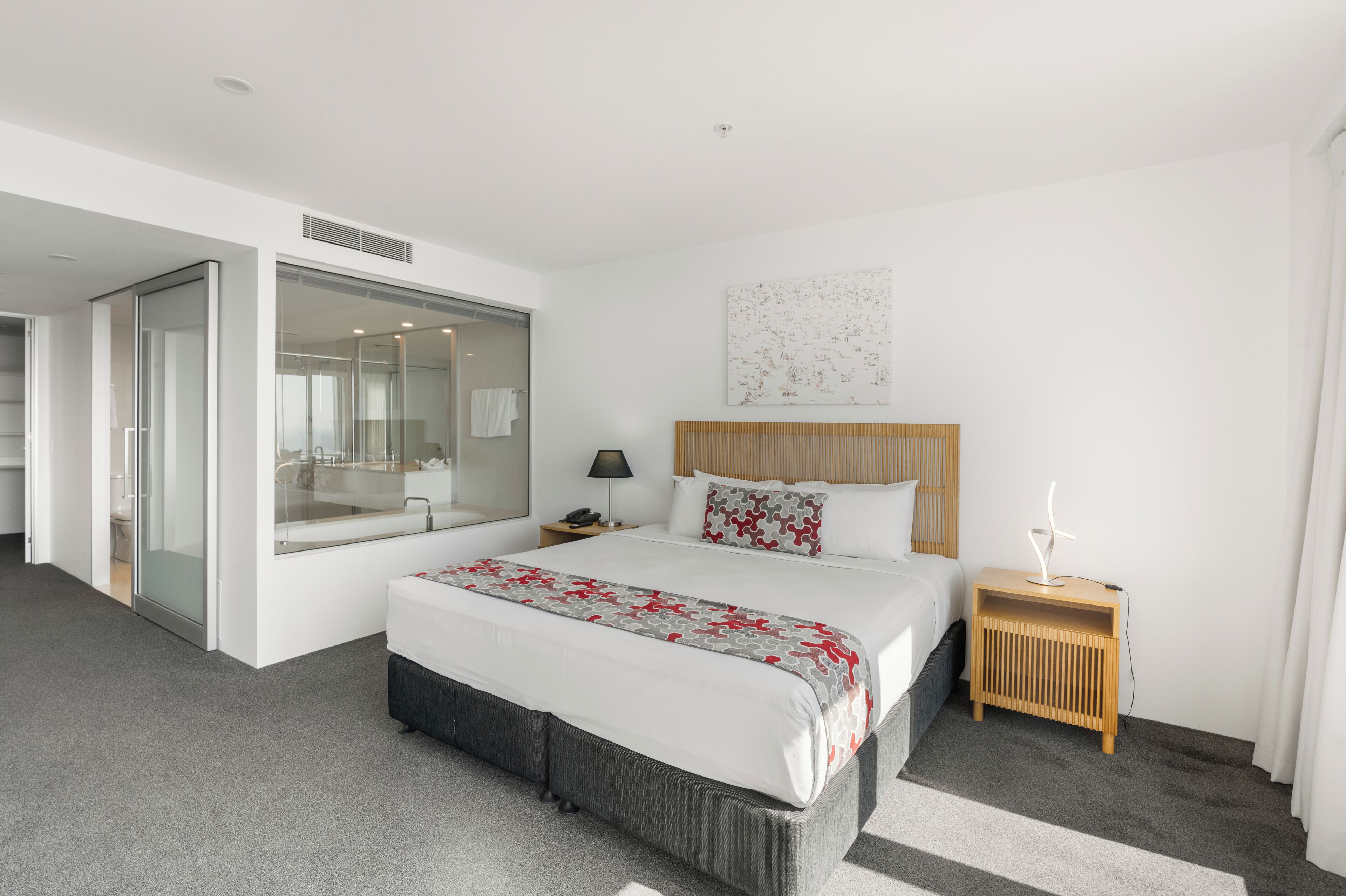 Una habitación de hotel moderna con una cama grande, una mesita de noche, un espejo y una puerta corredera que da a un baño.