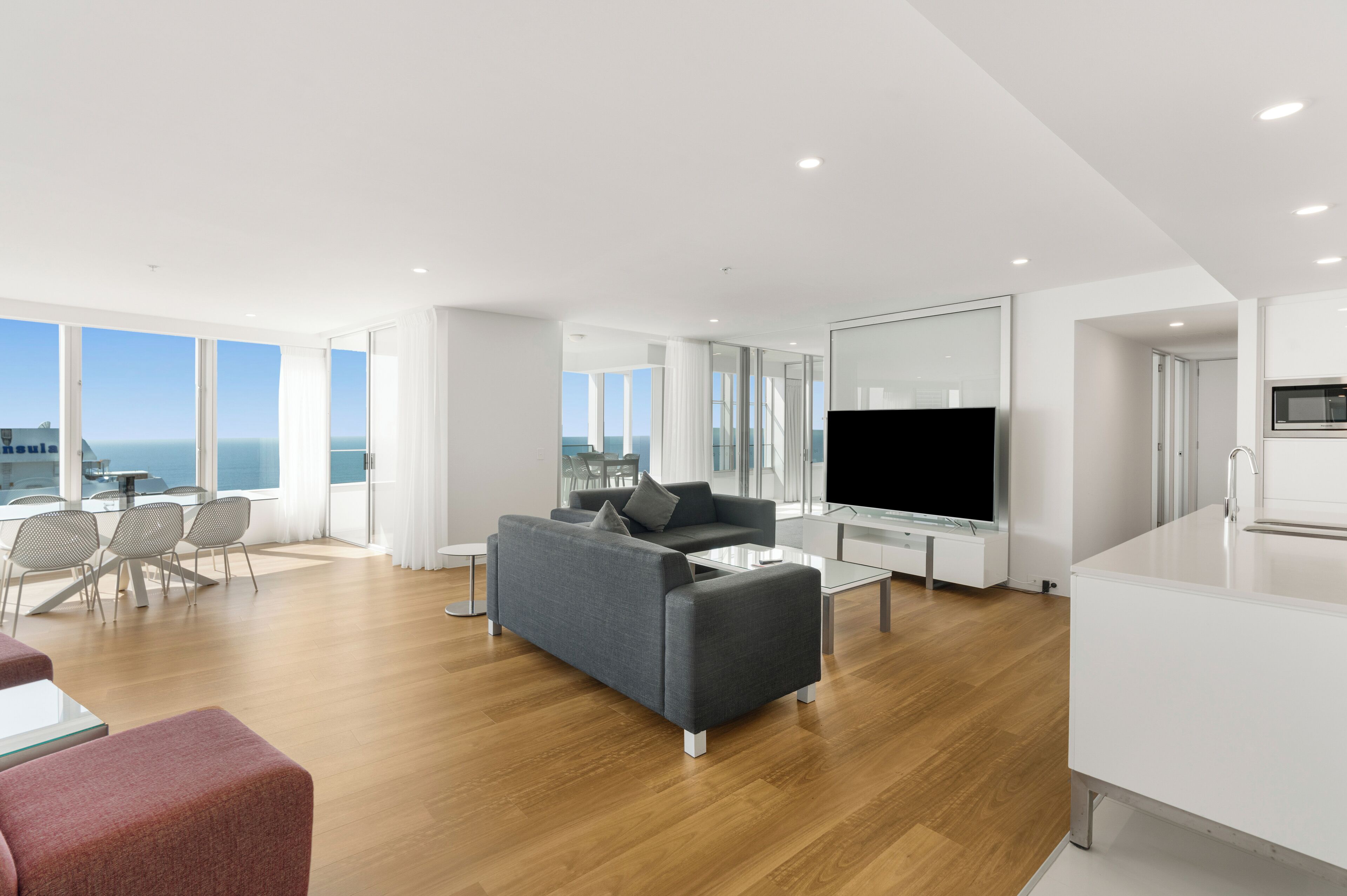A modern living room with a grey sofa, a flat-screen TV, and a dining area with a table and chairs.
