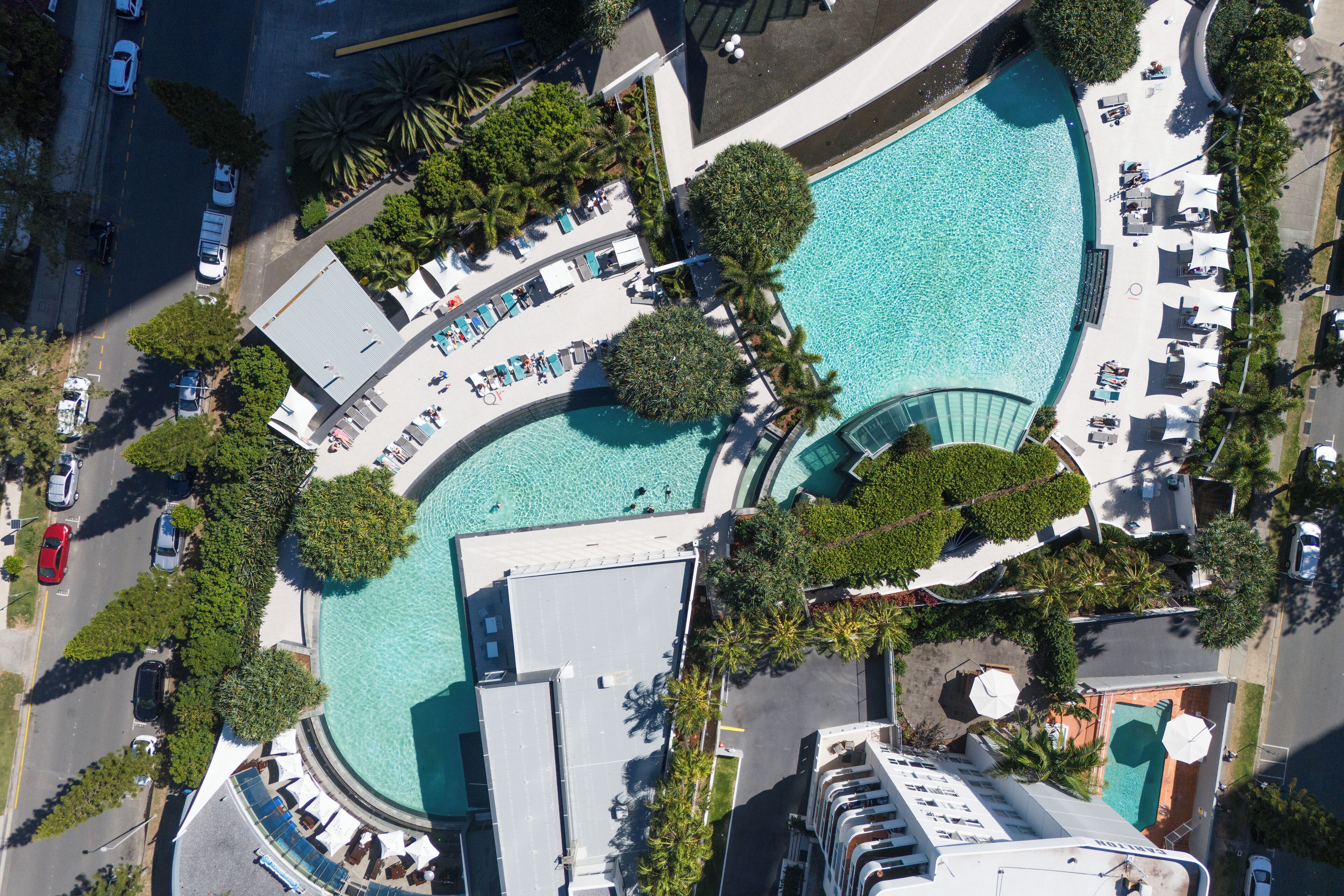 Vue aérienne d’un hôtel doté d’une grande piscine, de transats et d’un espace extérieur couvert.