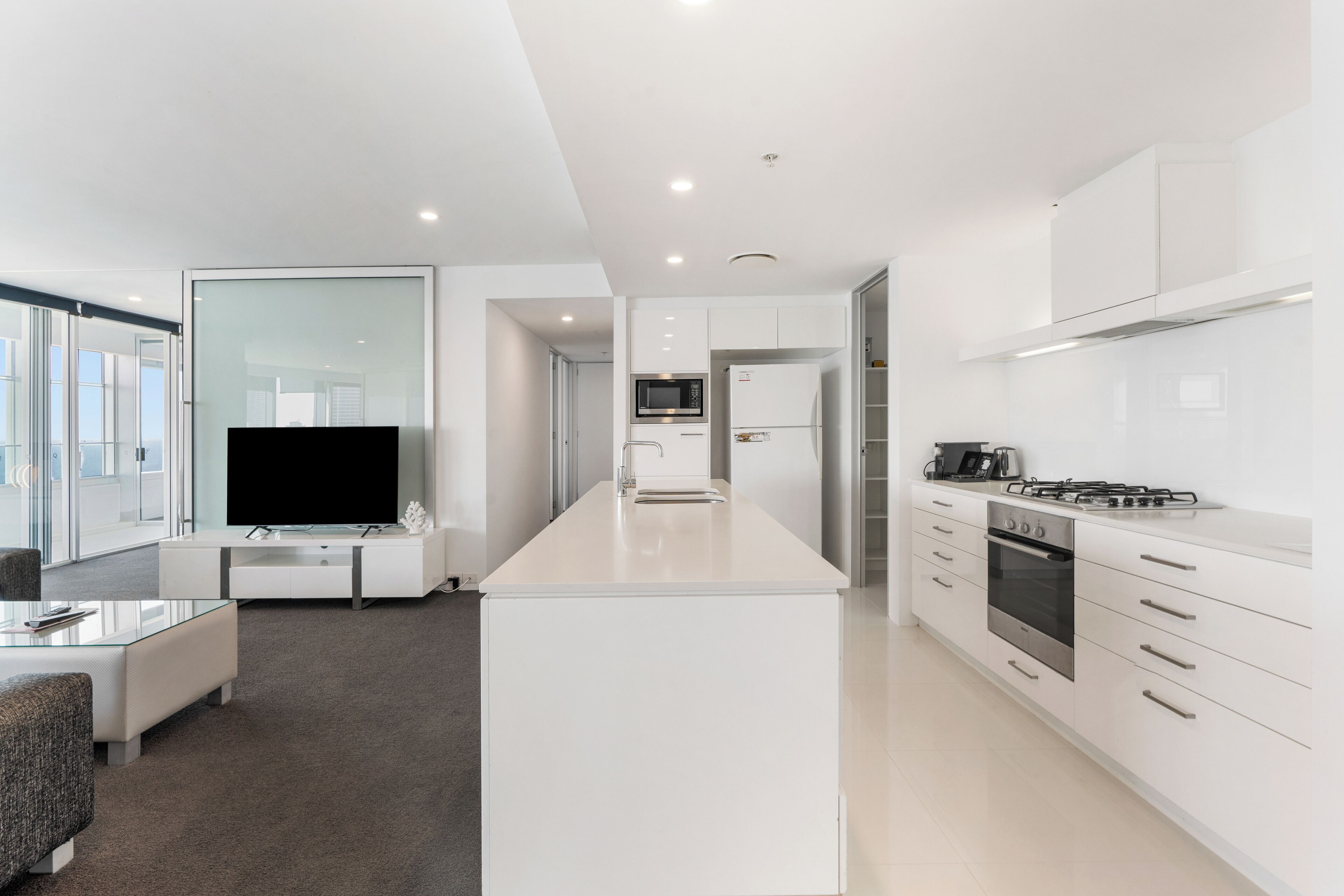 Una cocina moderna con armarios blancos, una isla central, horno empotrado y microondas.