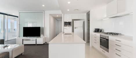 Una cocina moderna con armarios blancos, una isla central, horno empotrado y microondas.