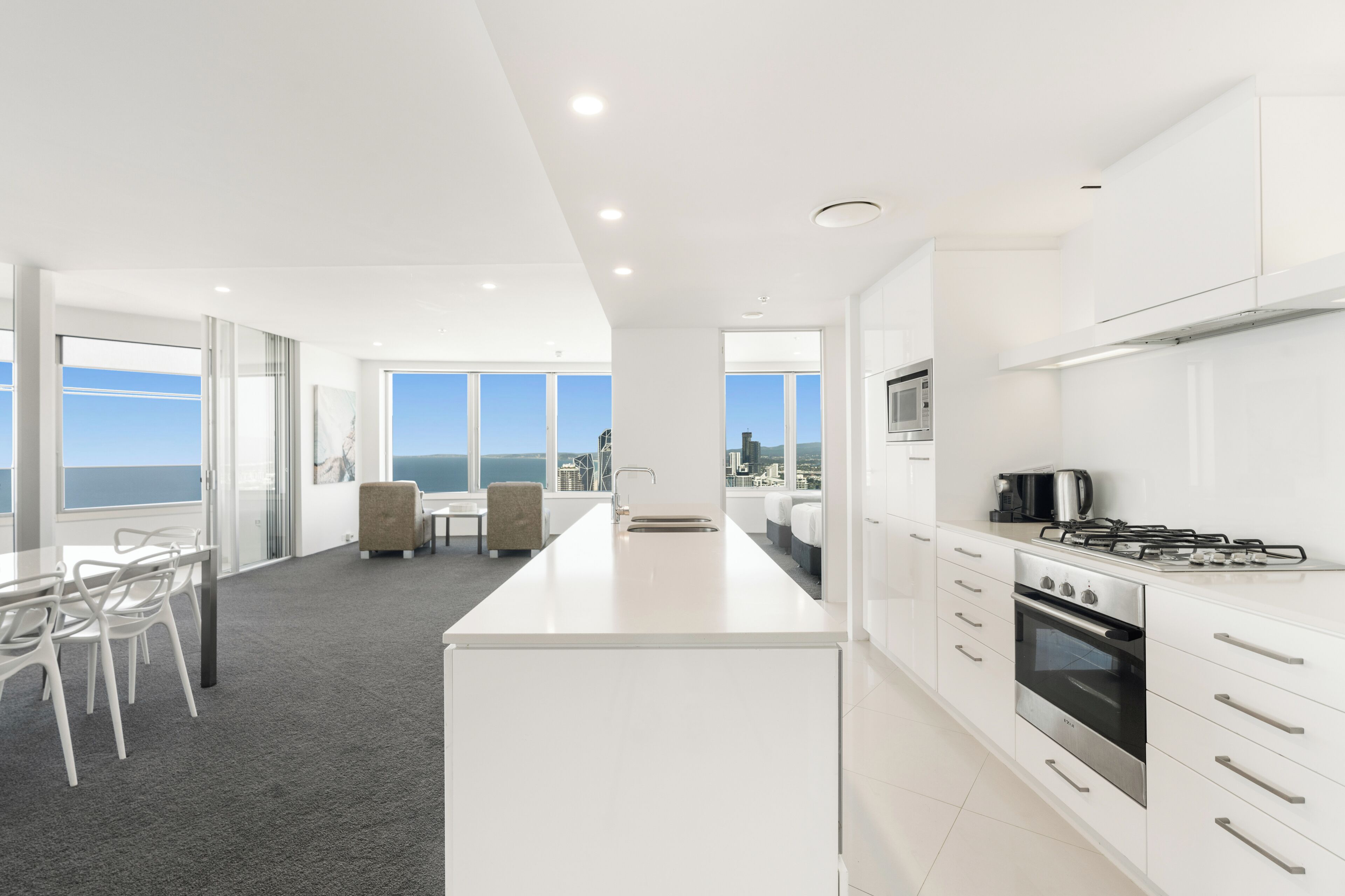 A modern kitchen with white cabinetry, a central island with a sink, and a view of the ocean through large windows.